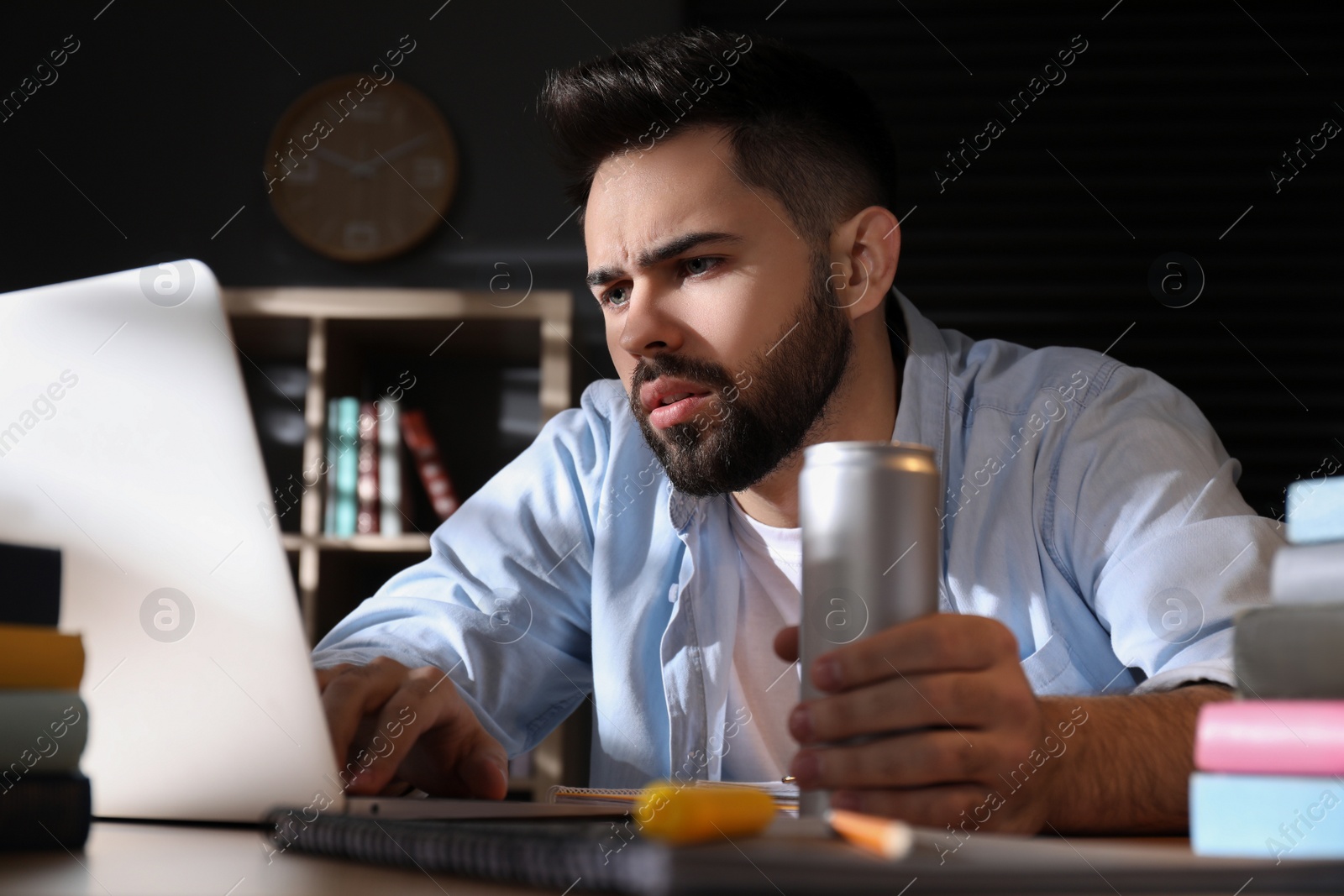 Photo of Tired young man with energy drink studying at home