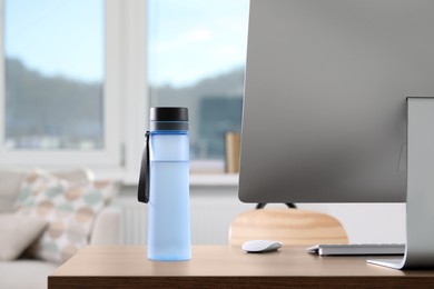 Stylish bottle of water and computer on table at workplace in office