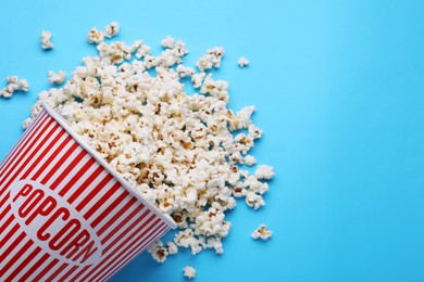 Photo of Overturned paper bucket with delicious popcorn on light blue background, flat lay. Space for text