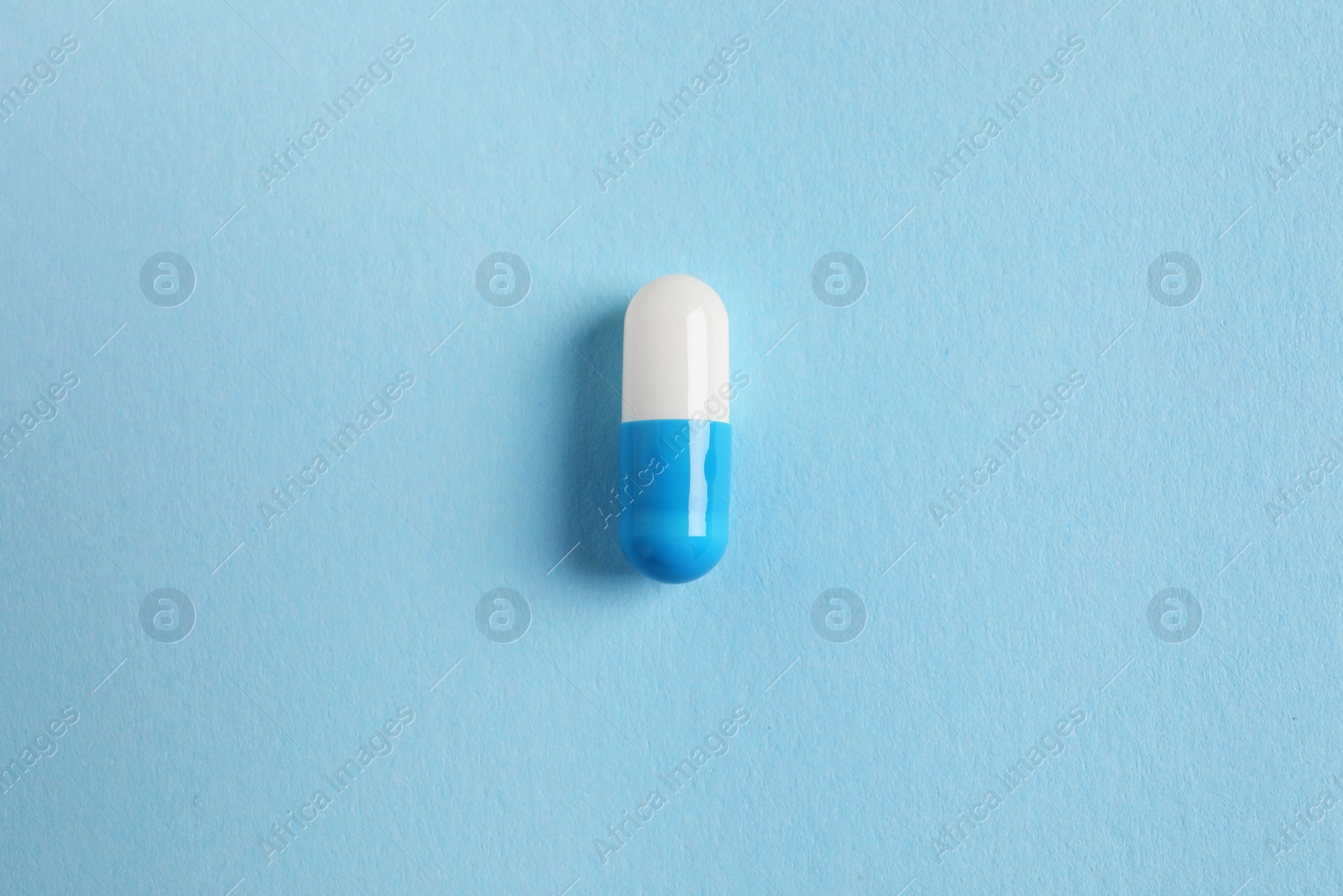 Photo of One colorful pill on light blue background, top view