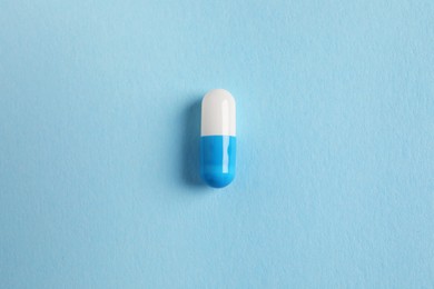 One colorful pill on light blue background, top view