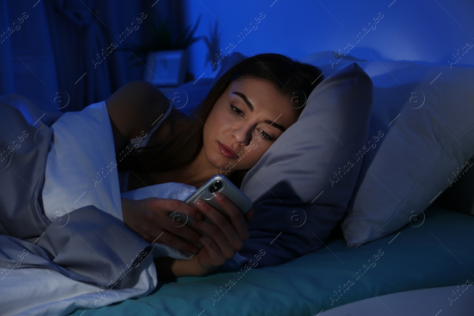 Photo of Young woman with mobile phone at night. Bedtime