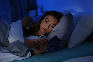 Young woman with mobile phone at night. Bedtime