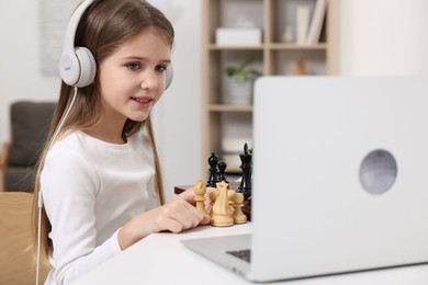 Photo of Cute girl learning to play chess with online tutor at home