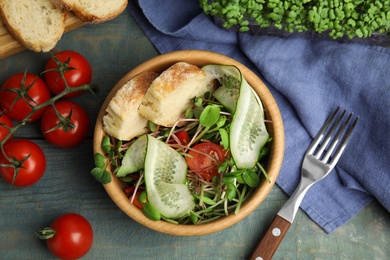 Salad with fresh organic microgreen in bowl on wooden table, flat lay