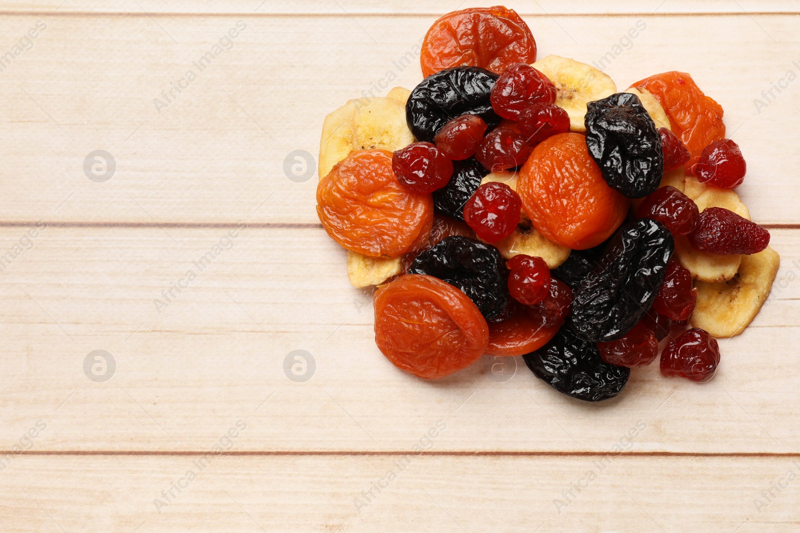 Photo of Mix of delicious dried fruits on white wooden table, top view. Space for text