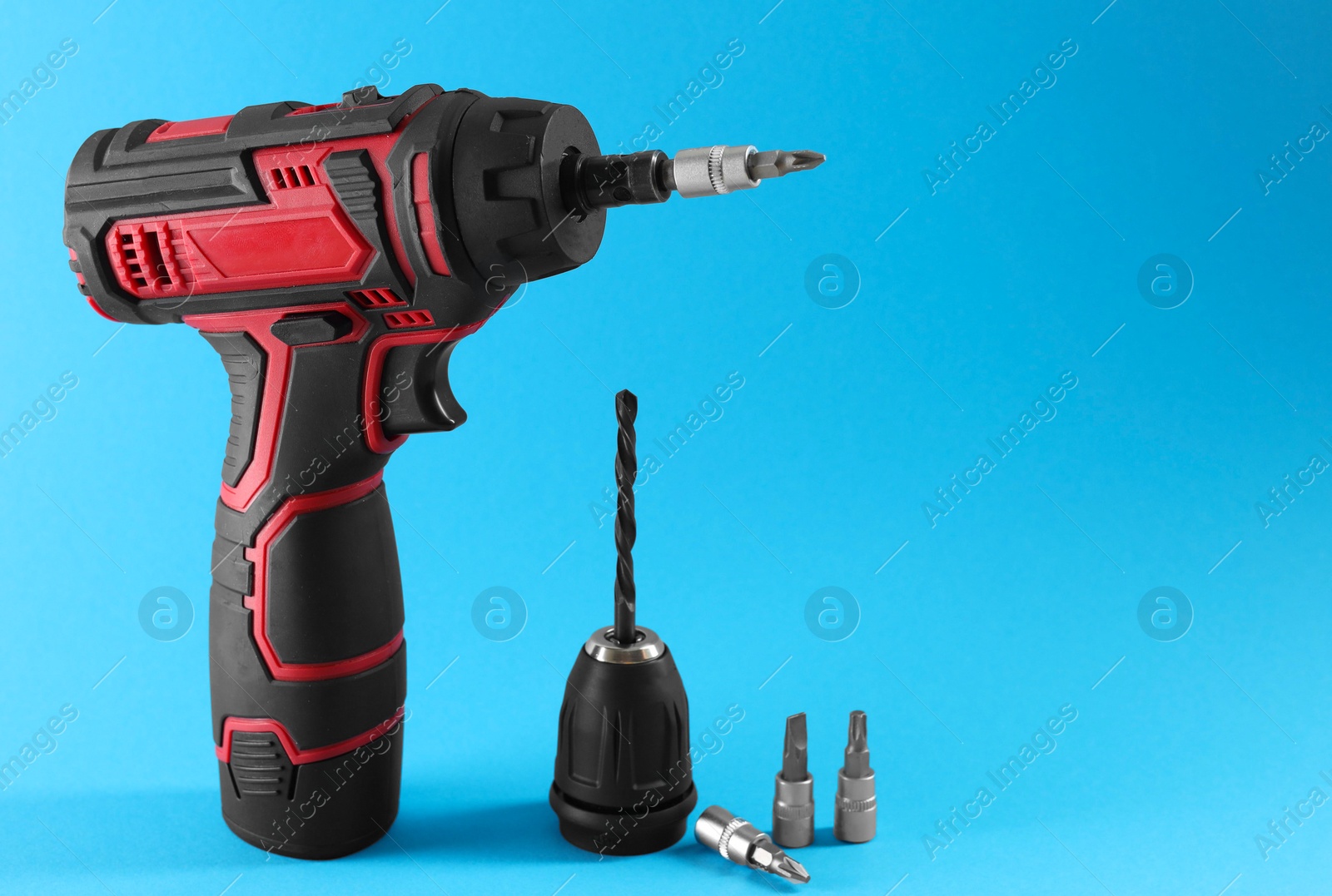 Photo of Modern electric screwdriver and drill bits on light blue background. Space for text