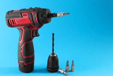 Modern electric screwdriver and drill bits on light blue background. Space for text
