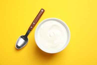 Bowl with creamy yogurt and spoon on color background, top view