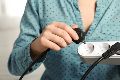 Woman inserting power plug into extension cord indoors, closeup. Electrician's professional equipment