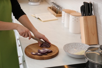 Photo of Woman cutting red onion into slices at table in kitchen, closeup