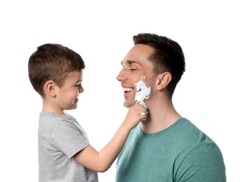 Photo of Little son applying shaving foam onto dad's face against white background