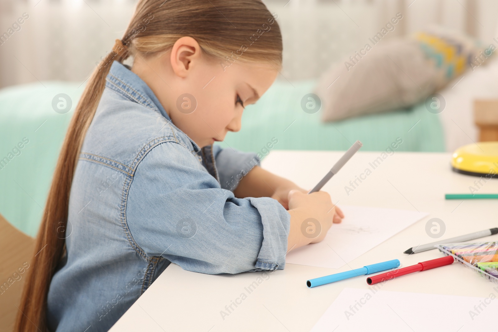 Photo of Cute little girl drawing with marker at desk in room. Home workplace