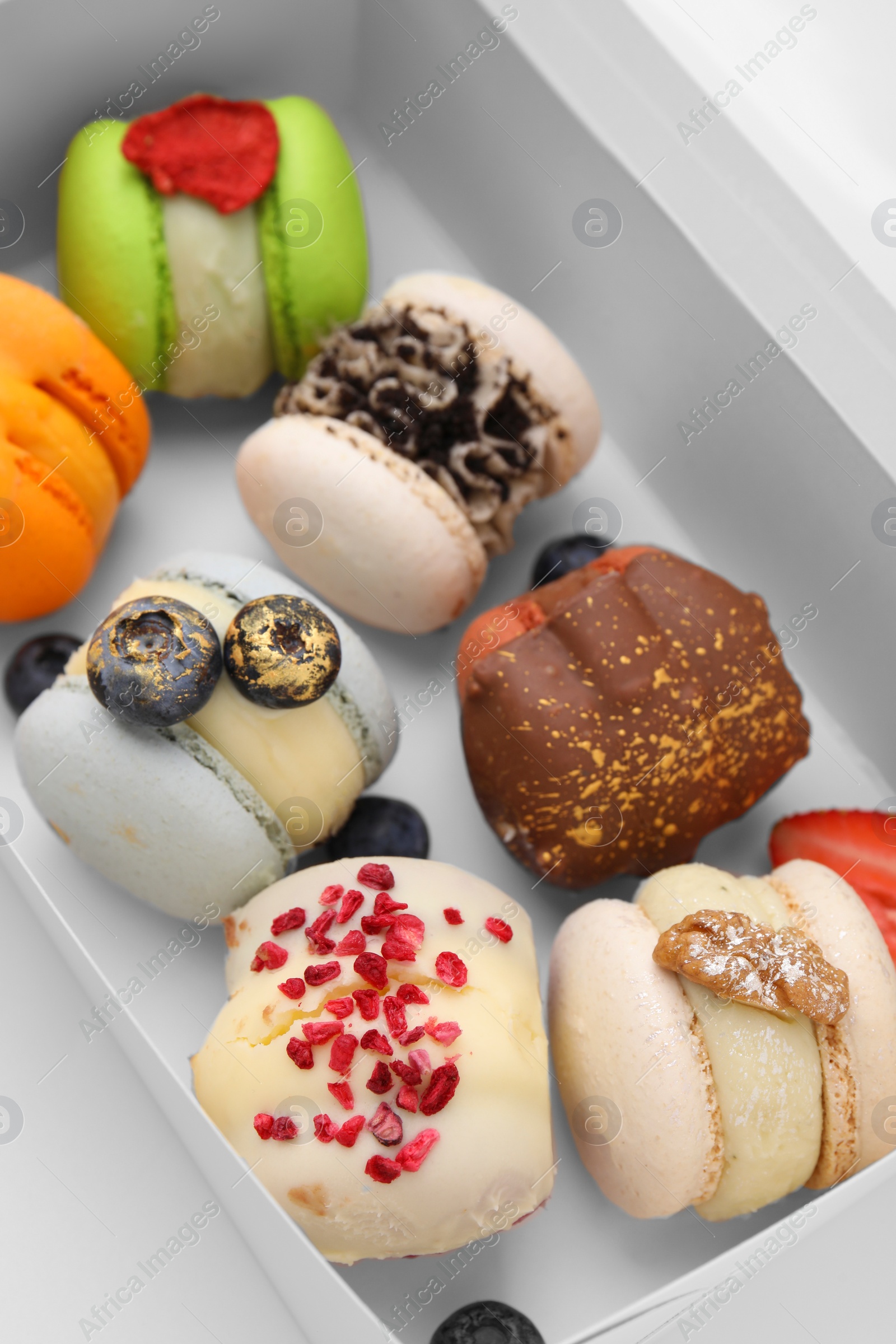 Photo of Cardboard box with delicious sweet macarons on white table, closeup