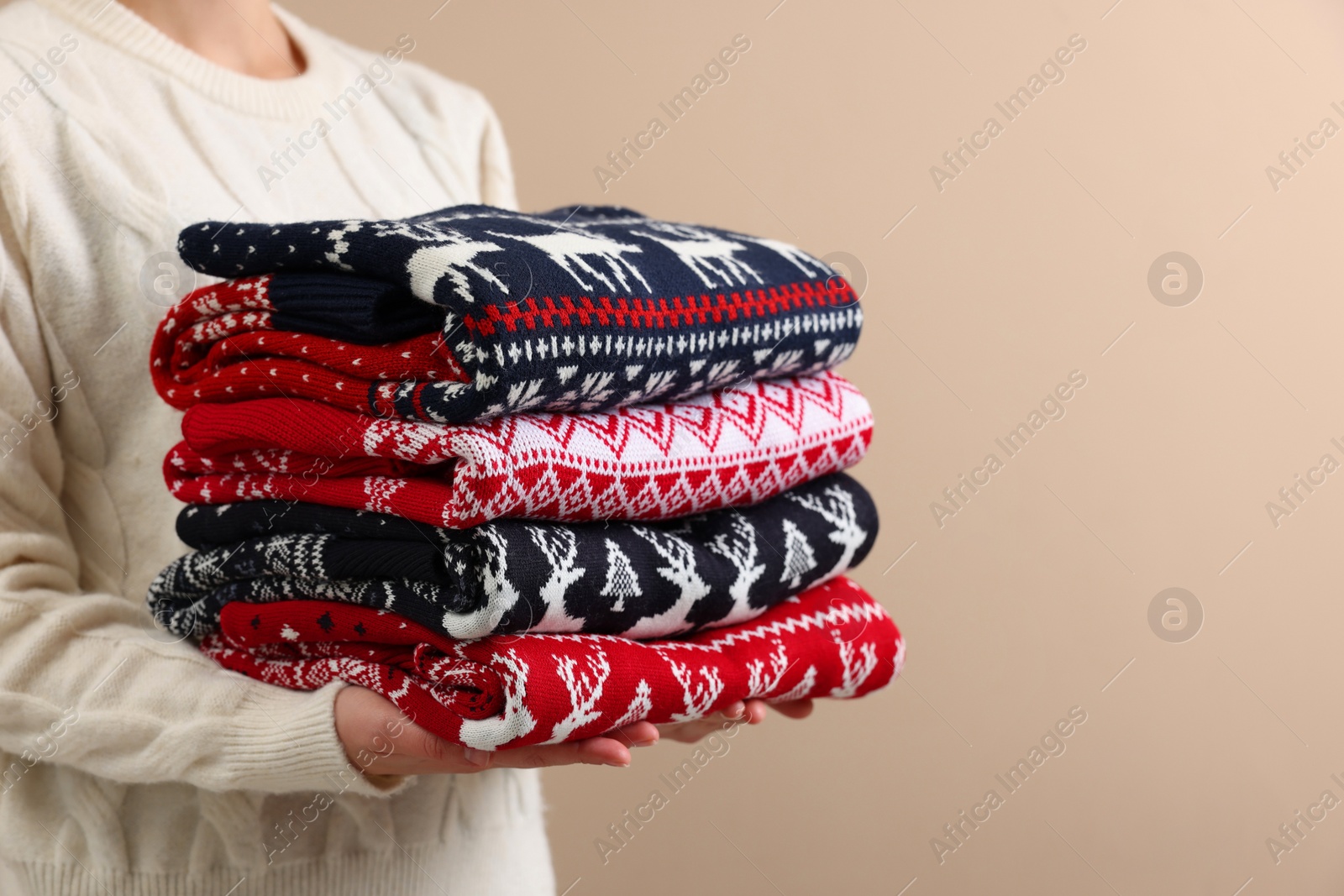 Photo of Woman holding stack of different Christmas sweaters on beige background, closeup. Space for text