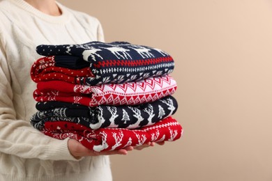 Photo of Woman holding stack of different Christmas sweaters on beige background, closeup. Space for text