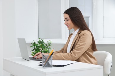 Photo of Young female intern working with laptop at table in office