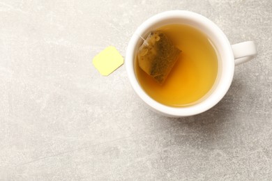 Photo of Brewing tea. Cup with tea bag on light table, top view. Space for text