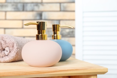 Stylish soap dispensers and towel on table against blurred background. Space for text