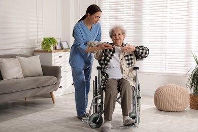 Photo of Senior woman in wheelchair doing physical exercise and young caregiver helping her indoors. Home health care service