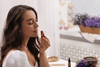 Beautiful young woman with bottle of essential oil indoors