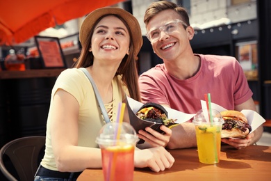 Photo of Young happy couple with burgers in street cafe