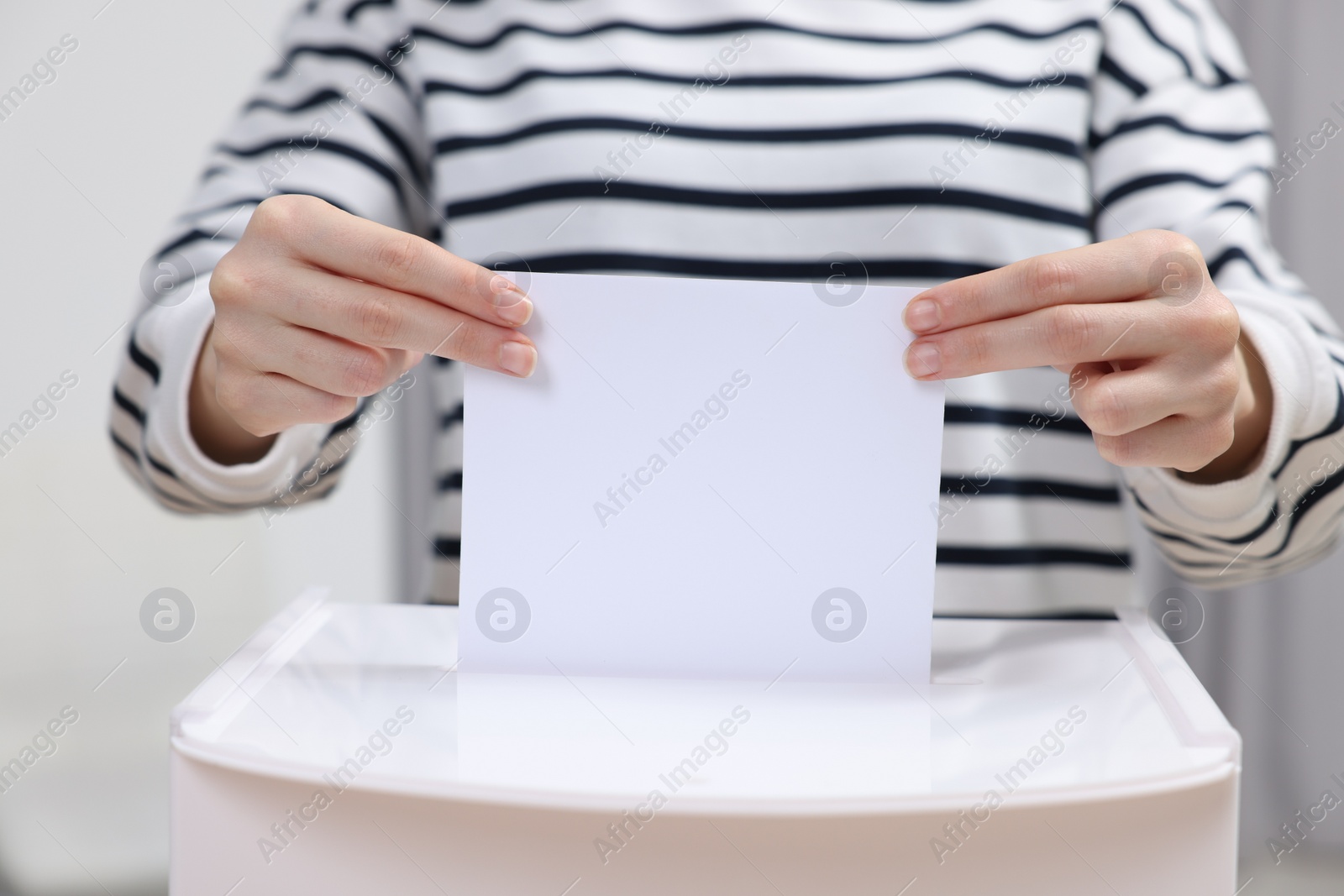 Photo of Woman putting her vote into ballot box on blurred background, closeup