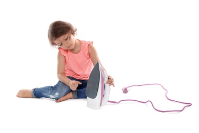 Photo of Little girl playing with iron on white background. Danger at home