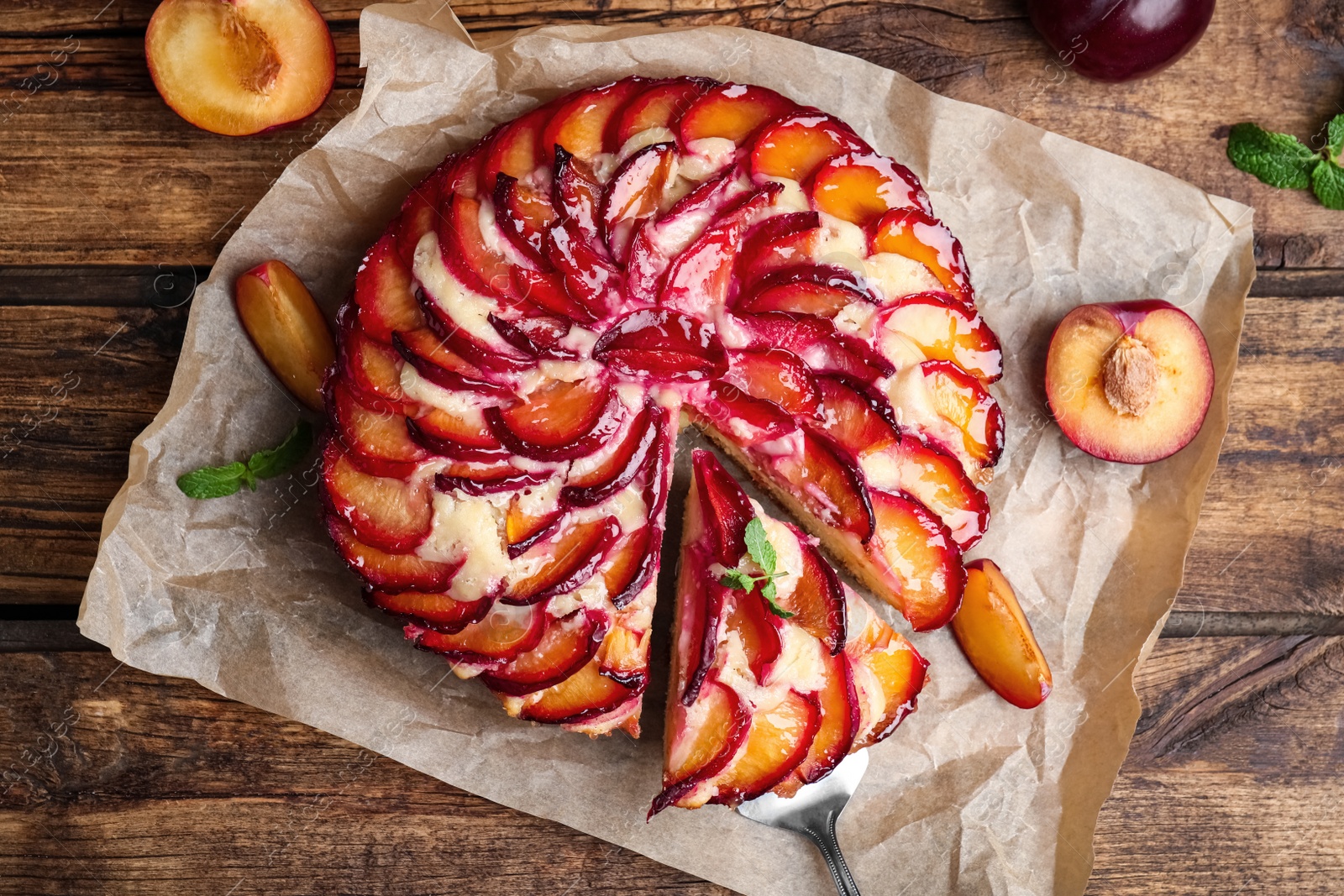 Photo of Delicious cake with plums on wooden table, flat lay