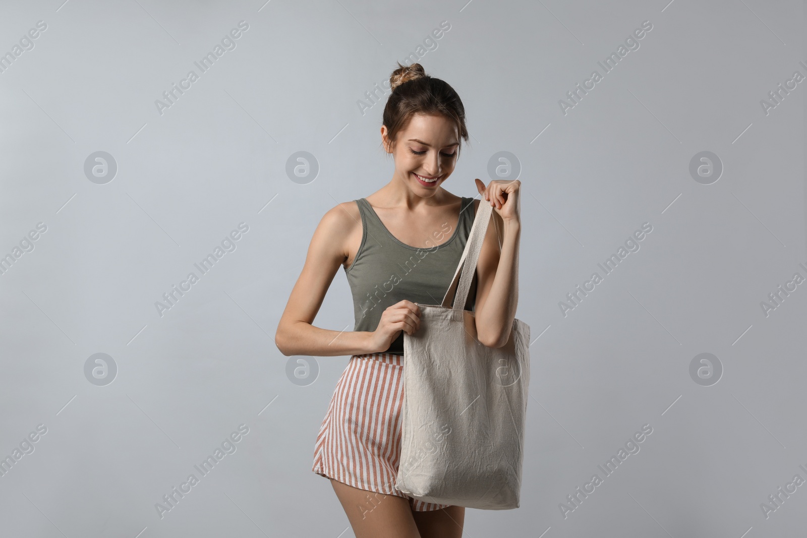 Photo of Happy young woman with blank eco friendly bag on light background