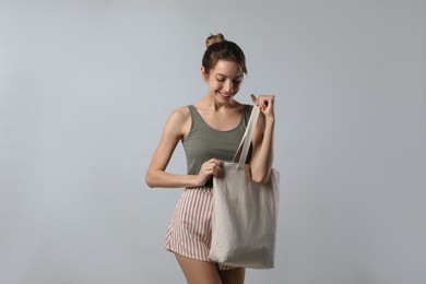 Photo of Happy young woman with blank eco friendly bag on light background