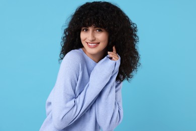 Happy young woman in stylish warm sweater on light blue background