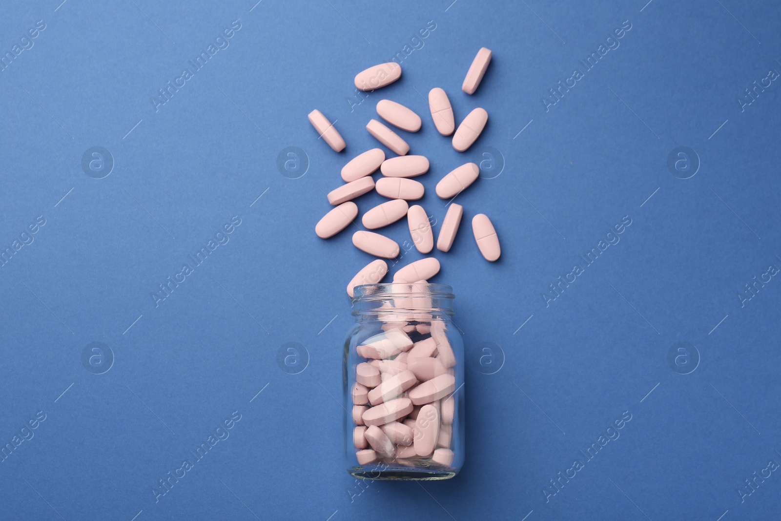 Photo of Bottle of pink vitamin capsules on blue background, top view