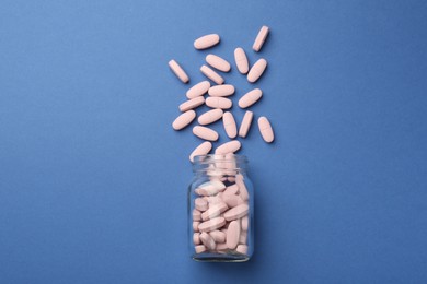 Photo of Bottle of pink vitamin capsules on blue background, top view