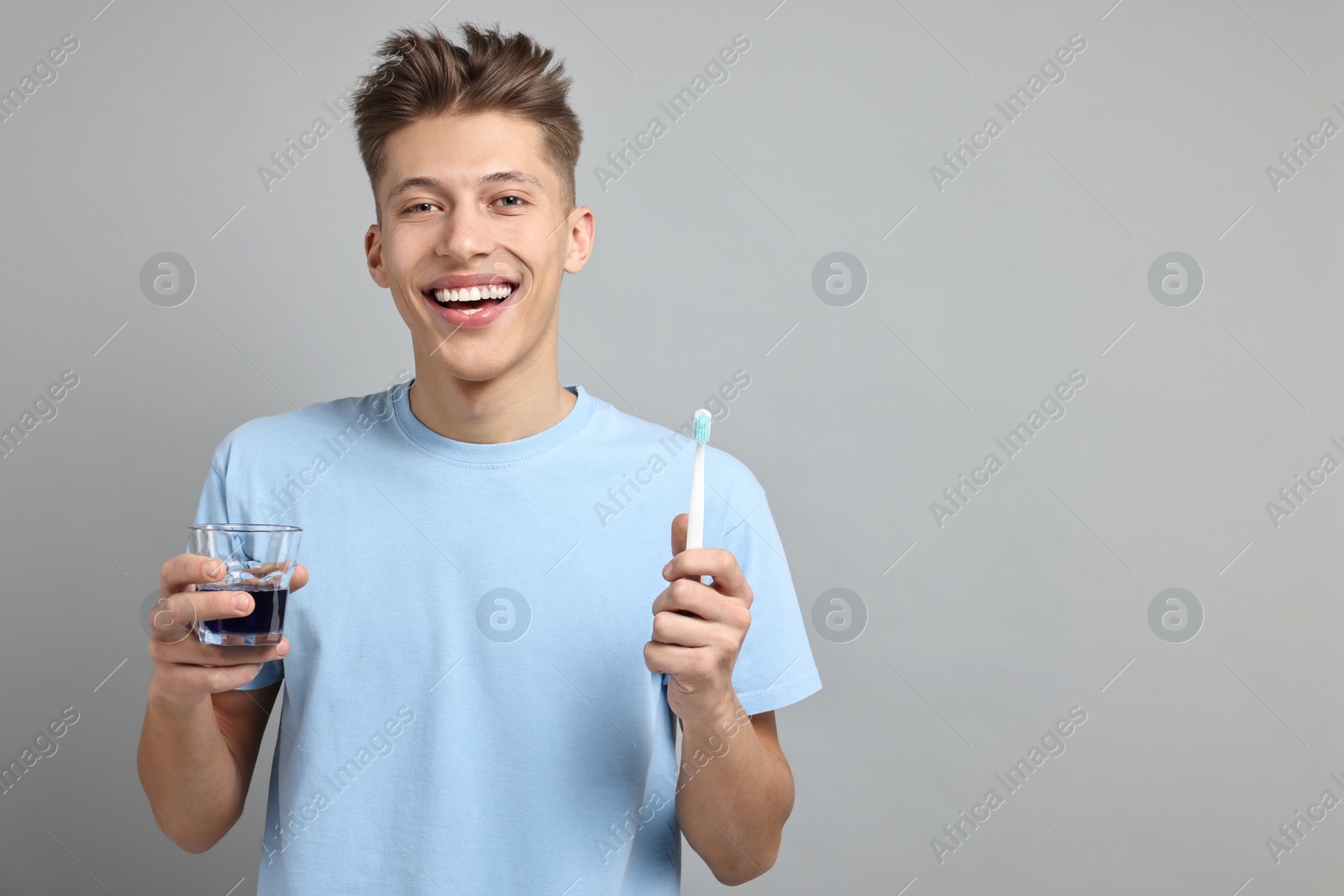 Photo of Young man with mouthwash and toothbrush on light grey background, space for text