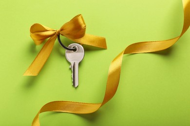 Photo of Key with yellow bow and ribbon on light green background, flat lay. Housewarming party