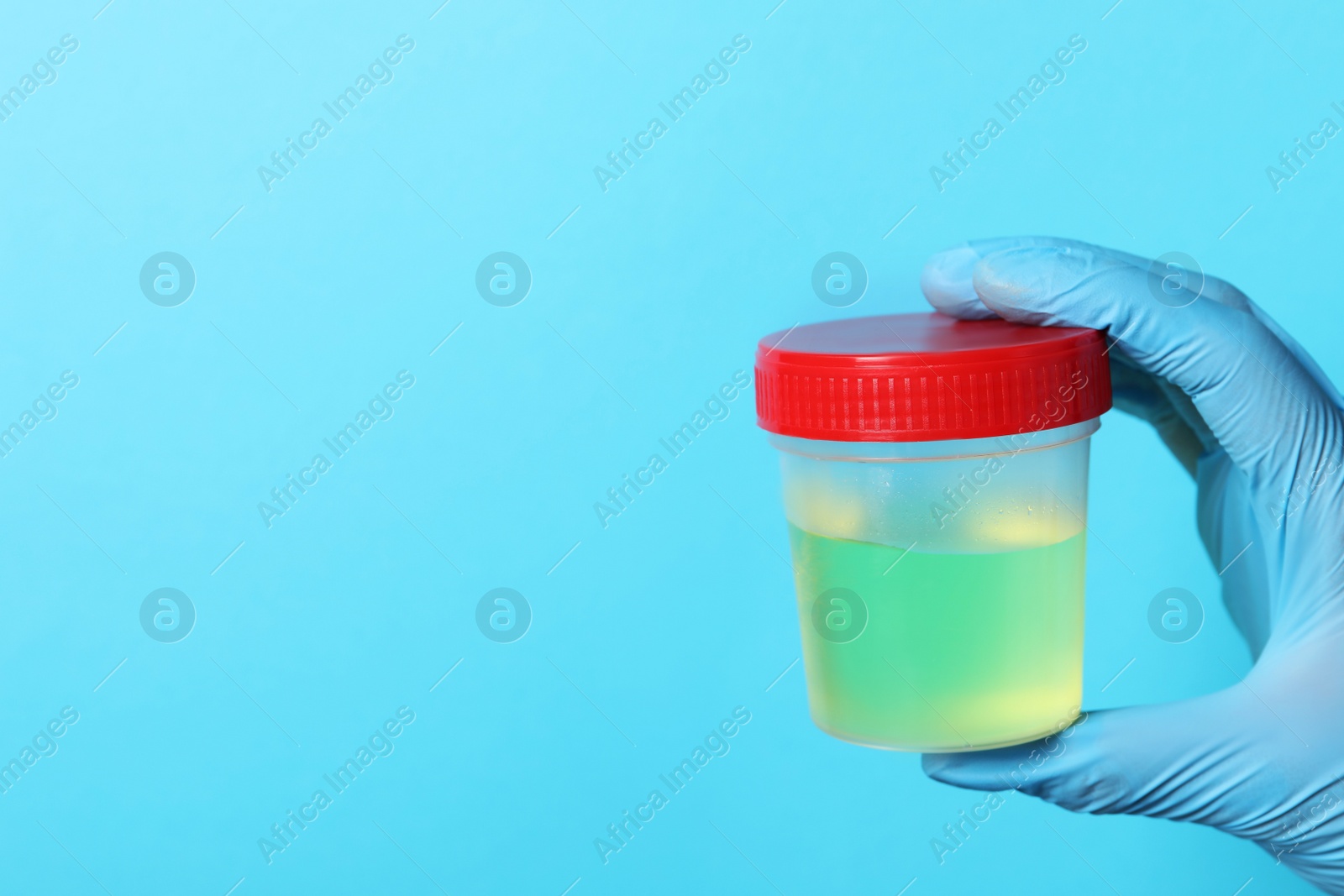 Photo of Doctor wearing glove holding container with urine sample for analysis on light blue background, closeup. Space for text