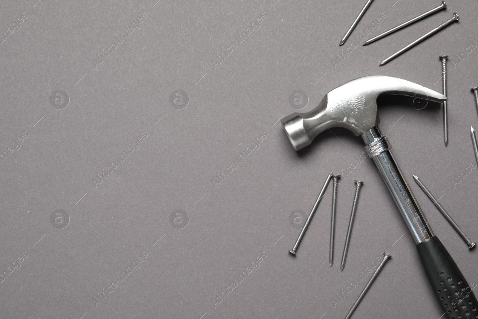 Photo of Hammer and metal nails on grey background, top view. Space for text