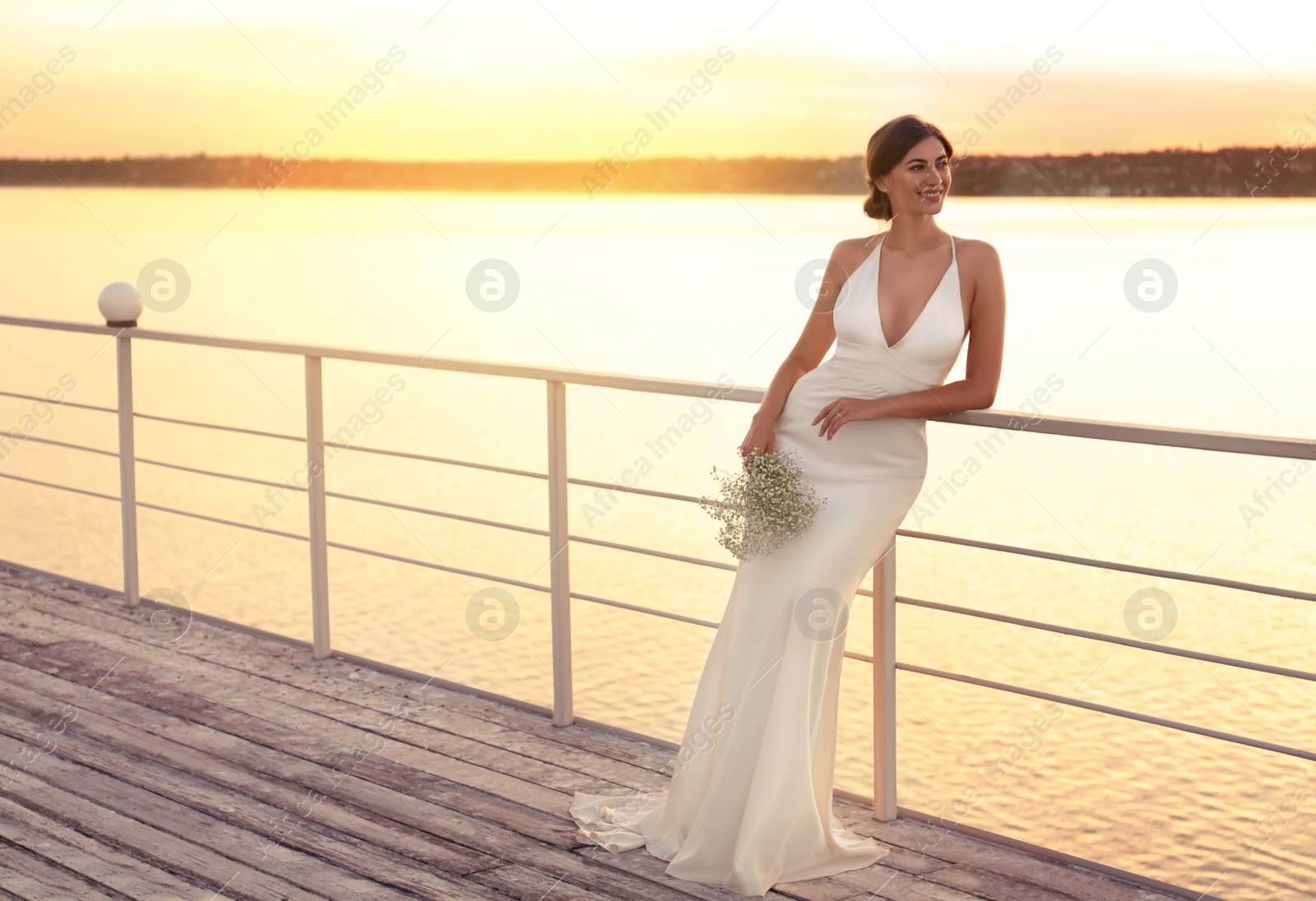 Photo of Gorgeous bride in beautiful wedding dress with bouquet near river on sunset. Space for text