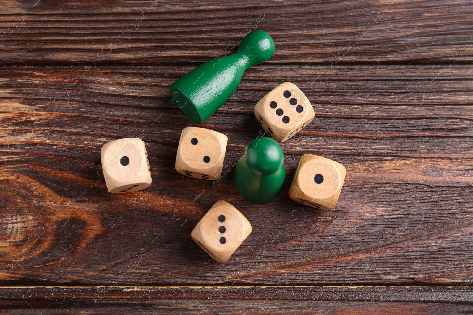 Photo of Many dices and green game pieces on wooden table, flat lay