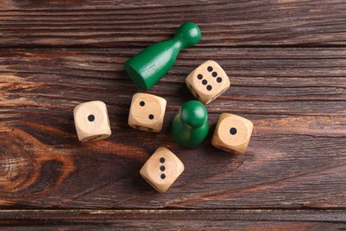 Many dices and green game pieces on wooden table, flat lay