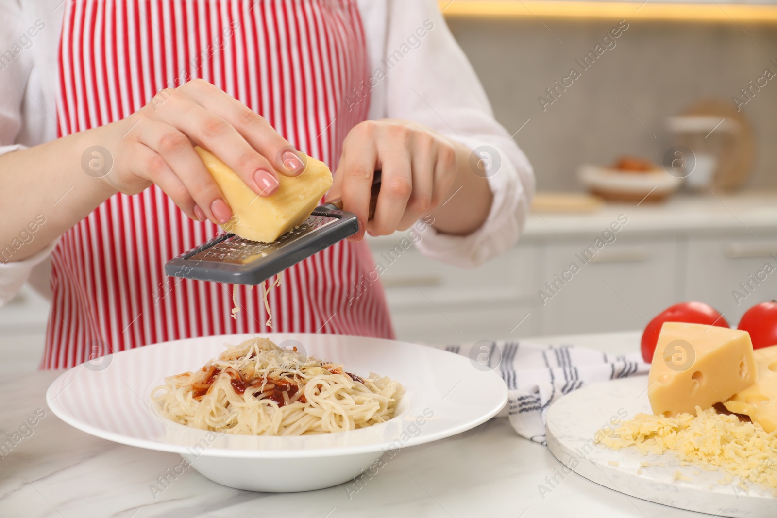 Photo of Woman grating cheese onto delicious pasta at white marble table in kitchen, closeup