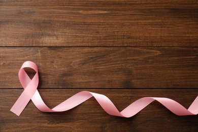 Pink ribbon on wooden table, top view with space for text. Breast cancer awareness concept