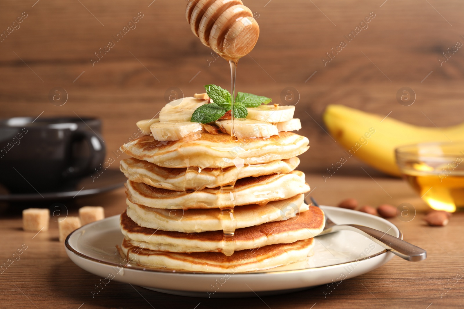 Photo of Pouring honey onto pancakes with sliced banana on wooden table