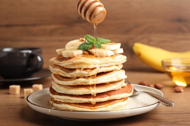 Photo of Pouring honey onto pancakes with sliced banana on wooden table