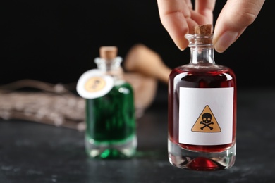 Photo of Woman holding glass bottle of poison with warning sign over table, closeup. Space for text