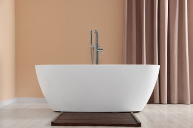 Stylish bathroom interior with ceramic tub near beige curtains