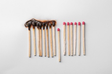 Photo of Burnt and whole matches on white background, flat lay