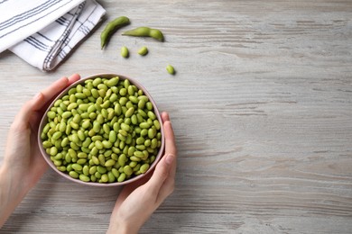 Woman holding bowl of edamame beans at light wooden table, closeup. Space for text