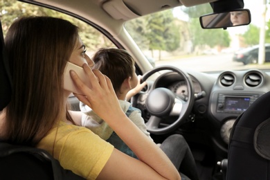 Mother with little son on knees driving car and talking by phone. Child in danger